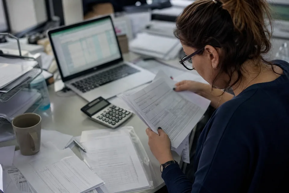 Finance specialist checking printed invoices against billing records with a calculator
