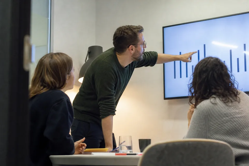 Small team reviewing a bar chart on a wall screen in a meeting room